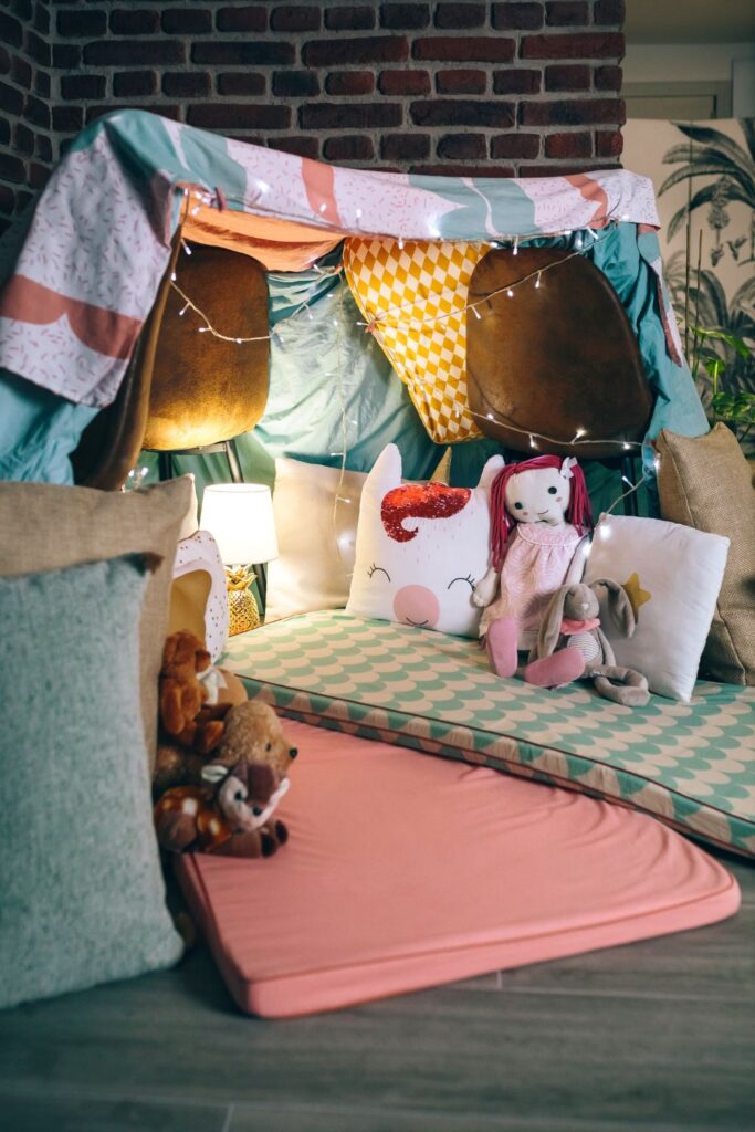 a fort built with blankets and a cushion with a unicorn stuffed animal.